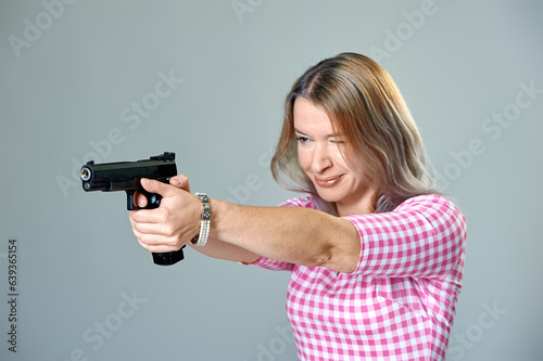 slender beautiful woman in a red dress with a gun in her hands on a gray background