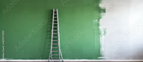 A partially painted wall and an aluminum ladder during a house renovation with a contrasting green and grey background