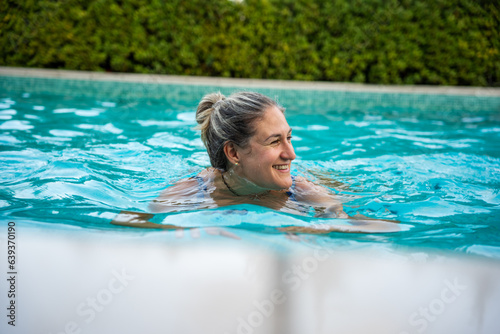 A smiling woman swimming in a pool in summer.