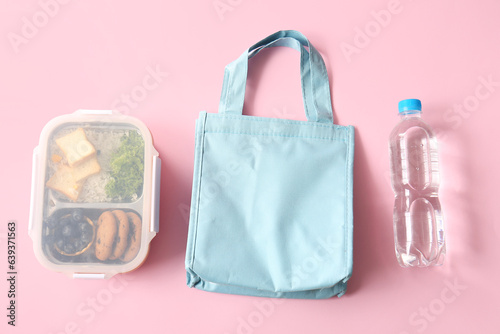 Bag, lunchbox with delicious food and bottle of water on pink background