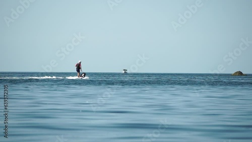 A motorized surfboard with a rider moving on a calm sea. The silhouette of a man on a water scooter glides through the water. Sports and sea activities on a beach holiday. Slow motion. photo