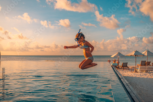Amazing sunset sea sky with joyful girl in snorkel gear jumping into pool. Tropical resort beach umbrellas, infinity poolside Excited funny little girl jumping to swimming pool. Happy summer vacation