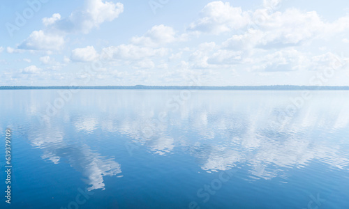 Fototapeta Naklejka Na Ścianę i Meble -  natural landscape, waterscape with large water body under a blue sky with clouds and a distant wooded shore