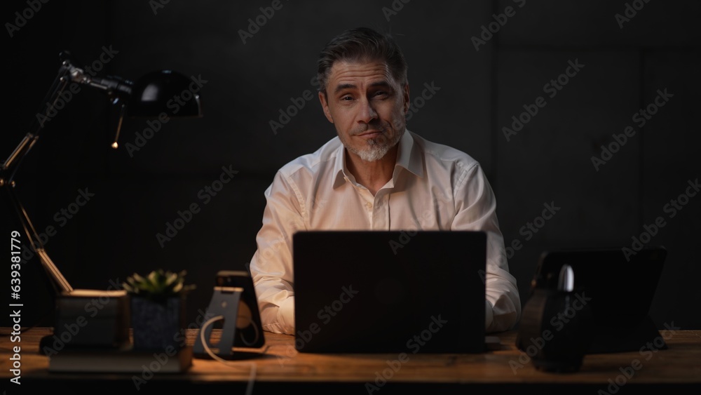 Businessman sitting at desk with laptop computer. Entrepreneur working late in office. Older, middle aged, mid adult, man in his 40s or 50s in business casual. Businessman sitting at desk with laptop computer. Entrepreneur working late in office. Older, middle aged, mid adult, man in his 40s or 50s in business casual.