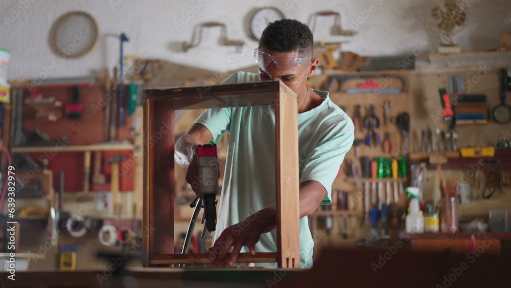Engaged in Craft scene of a Young Black Brazilian Carpenter Building Furniture at Workshop, apprentice using drilling equipment, wood carpentry student Engaged in Craft scene of a Young Black Brazilian Carpenter Building Furniture at Workshop, apprentice using drilling equipment, wood carpentry student
