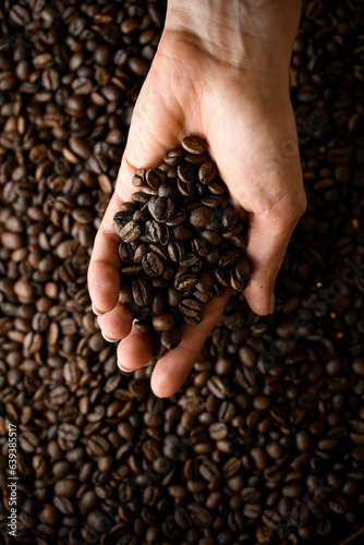 Top view of female hand holding freshly roasted fragnant coffee beans against background of other coffee beans