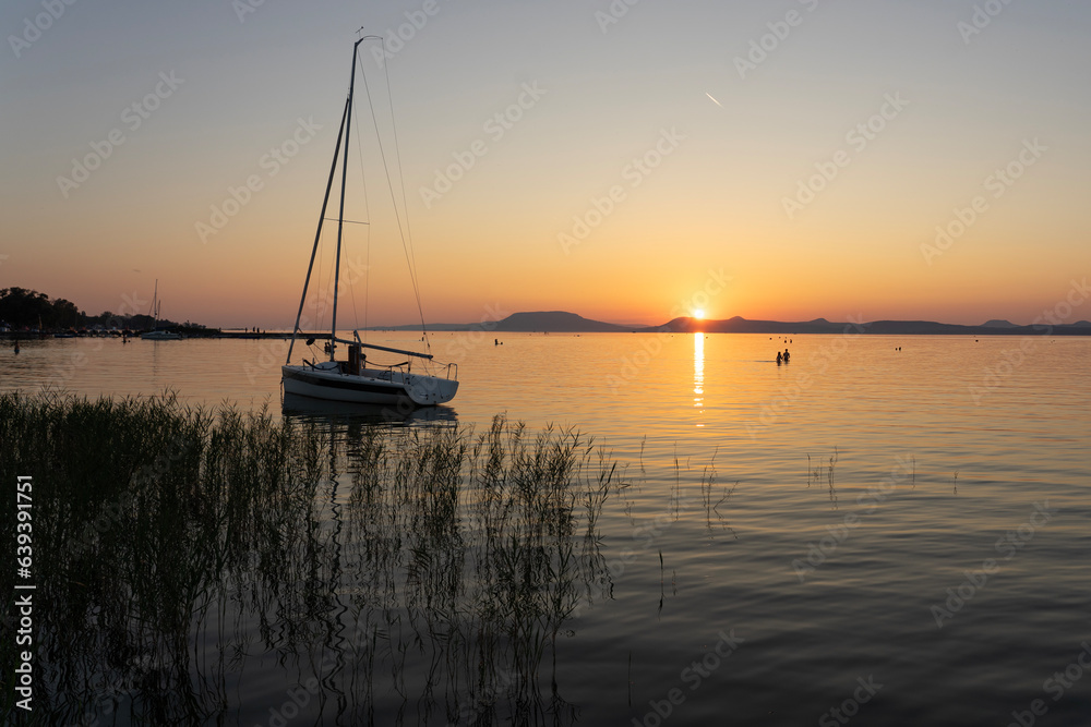 Lake Balaton at sunset with people and sailing ship silhouette and the north part mountains in the background
