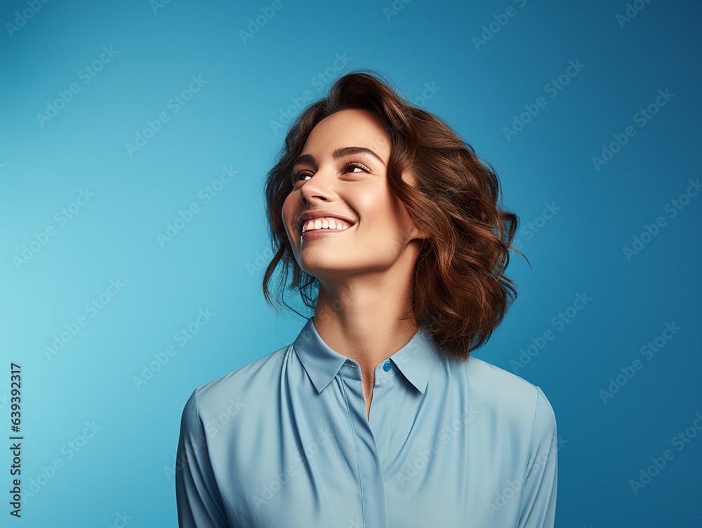 A cheerful and youthful woman stands confidently against a backdrop of solid color blue background A cheerful and youthful woman stands confidently against a backdrop of solid color blue background
