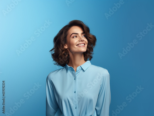 A cheerful and youthful woman stands confidently against a backdrop of solid color blue background