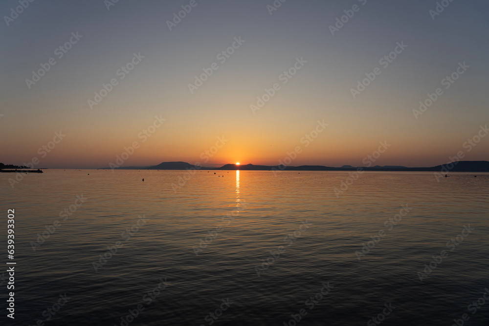 sunset at Lake Balaton with silhouette of night bathing people and the north part mountains in the background