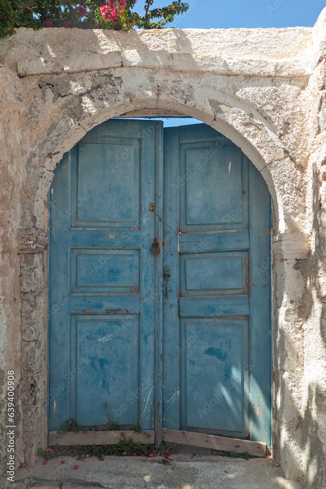 Traditional old wooden door of light blue color at an old house with ochre walls and stone threshold, in Oia village of Santorini, Greece.