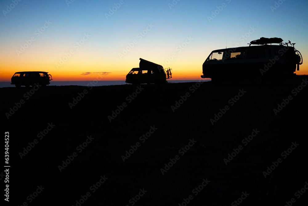 Fototapeta premium silhouette of camper vans parking on cliff during sunset 