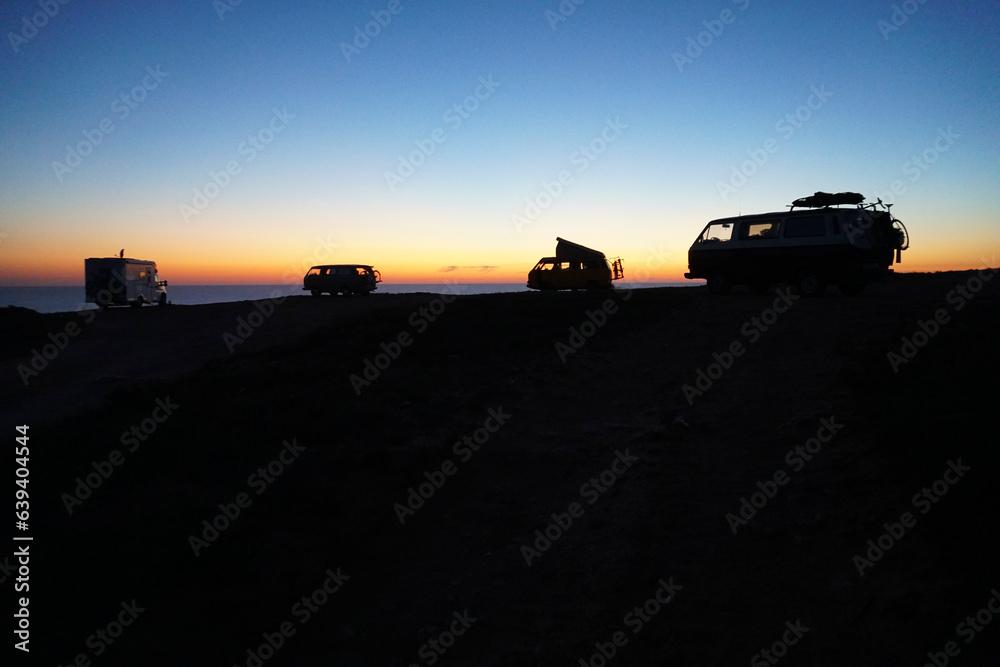 silhouette of camper vans parking on cliff during sunset silhouette of camper vans parking on cliff during sunset