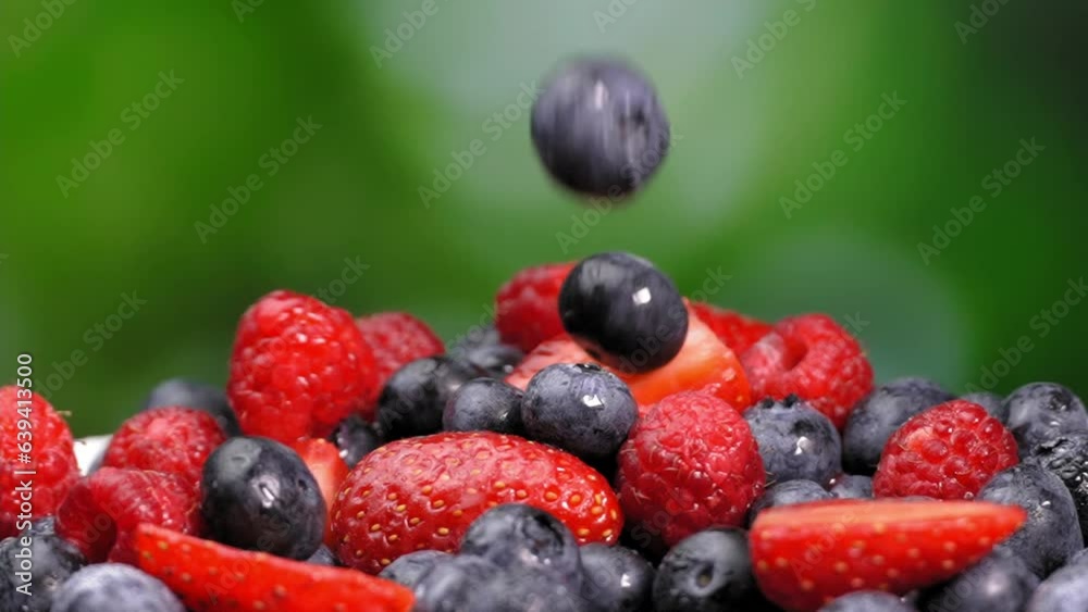 Wild blueberries, raspberries and strawberry slices spin on plate. Berries fly and fall into plate in slow motion on green background. Flying berries or throwing. Forest mix of wild berries. Harvest. Wild blueberries, raspberries and strawberry slices spin on plate. Berries fly and fall into plate in slow motion on green background. Flying berries or throwing. Forest mix of wild berries. Harvest.