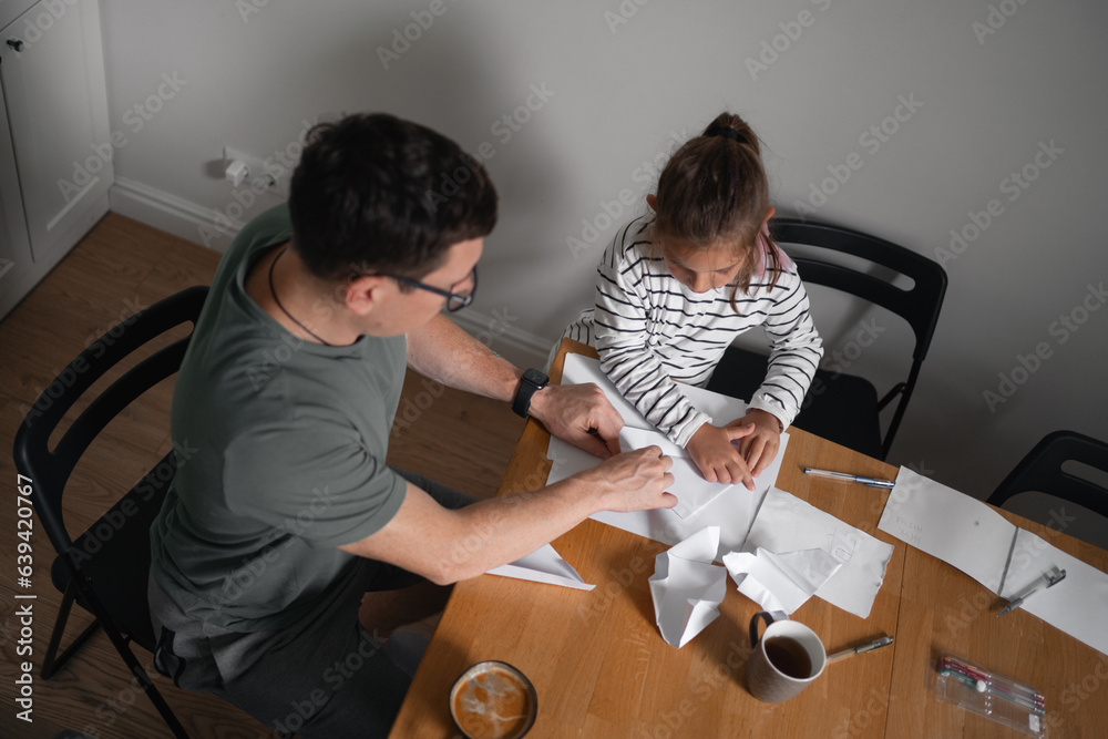 Father and child girl doing origami crafts together. Modern parenthood, weekend education activities at home of parents with children. Father and child girl doing origami crafts together. Modern parenthood, weekend education activities at home of parents with children.