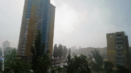 Rain and snow against the background of houses in the city. Heavy snowstorm on city streets. Silhouettes of high-rise buildings in the snow. Trees sway in the wind near the highway with cars. Fisheye