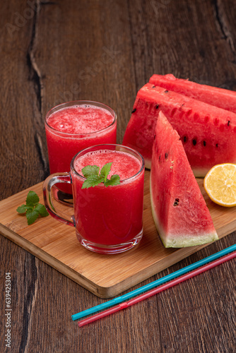 Watermelon squeezed juice, watermelon pieces and lemon on a wooden background.