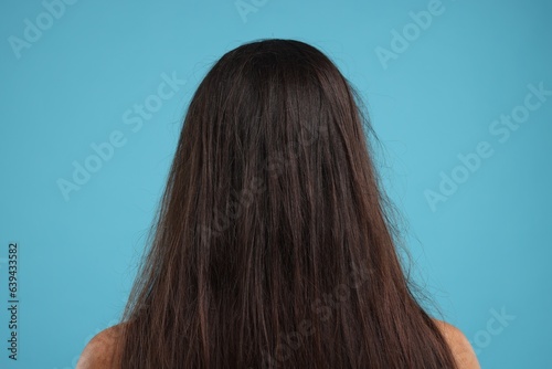 Woman with damaged messy hair on light blue background, back view