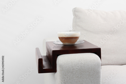 Cup of coffee on sofa with wooden armrest table indoors. Interior element photo