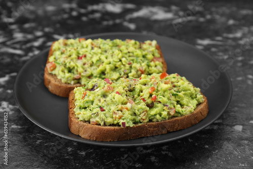 Slices of bread with tasty guacamole on black textured table, closeup
