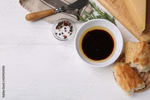 Bowl of balsamic vinegar with oil, bread and spices on white wooden table, flat lay. Space for text photo