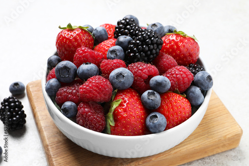 Many different fresh ripe berries in bowl on light grey table  closeup