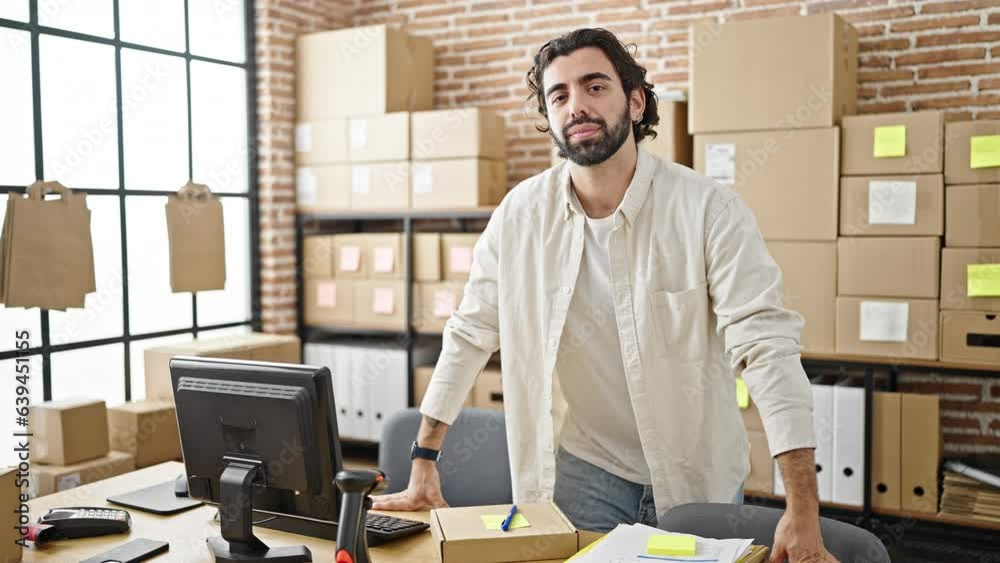 Young hispanic man ecommerce business worker standing by table with serious face at office Young hispanic man ecommerce business worker standing by table with serious face at office