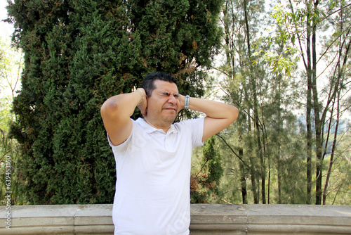 Dark-haired 40-year-old Latino man suffering from stress or migraine headache outdoors