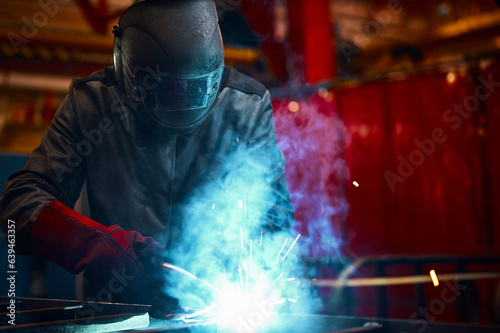 Employee in protective mask and gloves welds metal carcass
