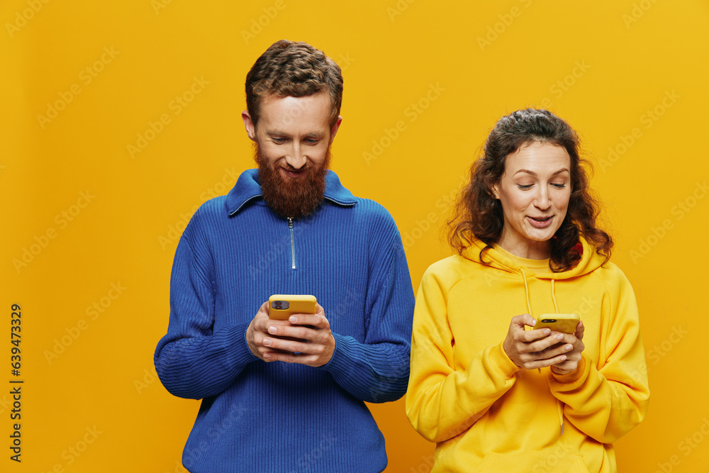Woman man cheerful couple with phones in hand social networking and communication crooked smile fun and fight, in yellow background. The concept of real family relationships, freelancers, work online. Woman man cheerful couple with phones in hand social networking and communication crooked smile fun and fight, in yellow background. The concept of real family relationships, freelancers, work online.