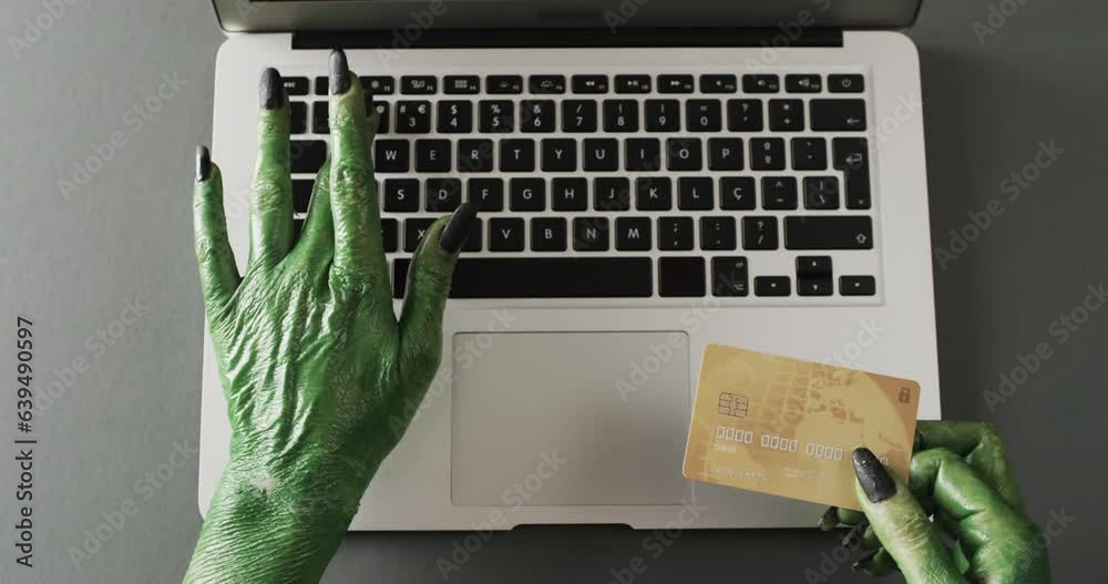 Video of halloween green monster hands holding card and laptop with copy space on grey background