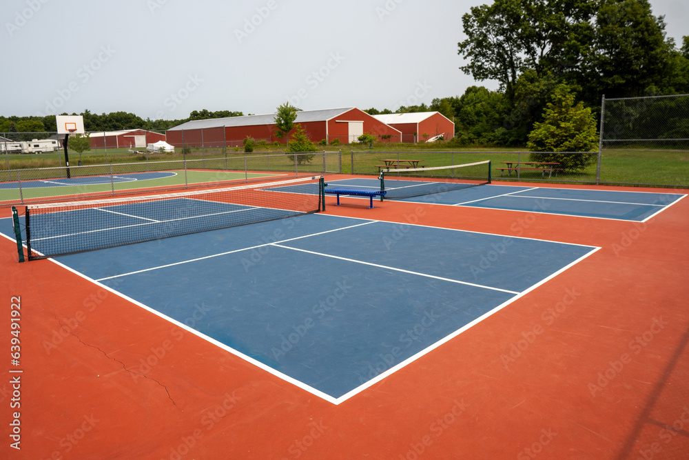 Fototapeta premium Recreational sport of pickleball court in Michigan, USA looking at an empty blue and orange clay colored court at a outdoor park.