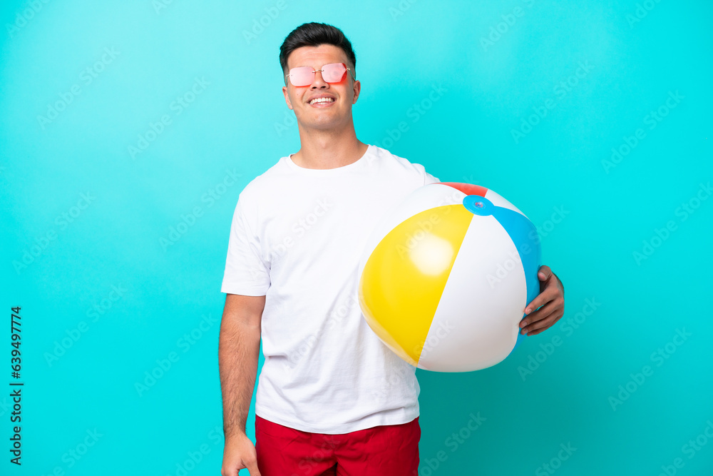 Young caucasian man holding a beach ball isolated on blue background thinking an idea while looking up