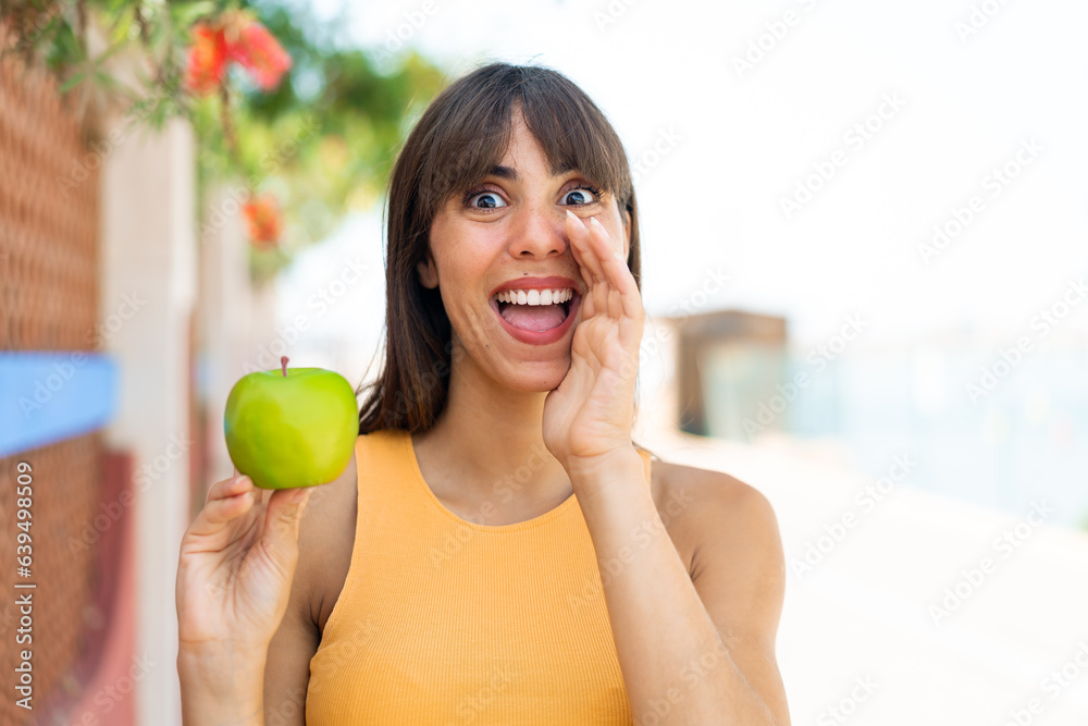 Young woman with an apple at outdoors shouting with mouth wide open Young woman with an apple at outdoors shouting with mouth wide open