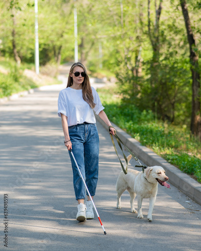 Blind woman walking with guide dog in the park. 