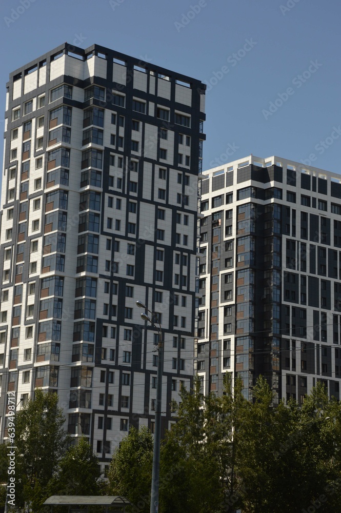 A high-rise gray building against a blue sky. Modern high-rise residential buildings in the city. Beautiful decoration of the facades of houses. Architecture.