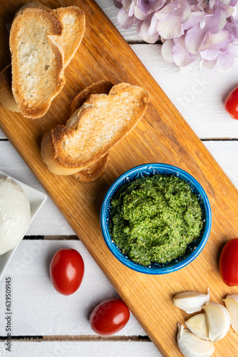 Traditional Italian pesto sauce served with mozzarella cheese, tomatoes and bruschetta on a white wooden table