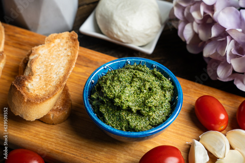 Traditional Italian pesto sauce served with mozzarella cheese, tomatoes and bruschetta on a dark wooden table