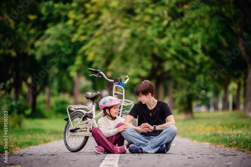 Young mother in jeans and black t-shirt teaching and sitting with her daughter on track in summer parks while speaking