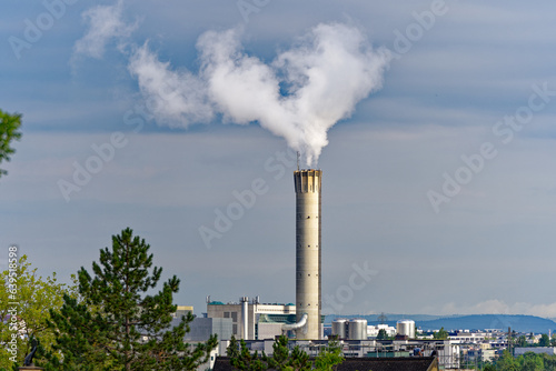 Concrete chimney of waste incineration plant with white smoke on a cloudy summer morning at City of Zürich, Switzerland.