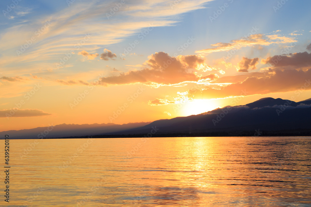 Obraz premium Colorful sunset on the sea. Mountain lake in the rays of the orange sun. Kyrgyzstan, Lake Issyk-Kul.
