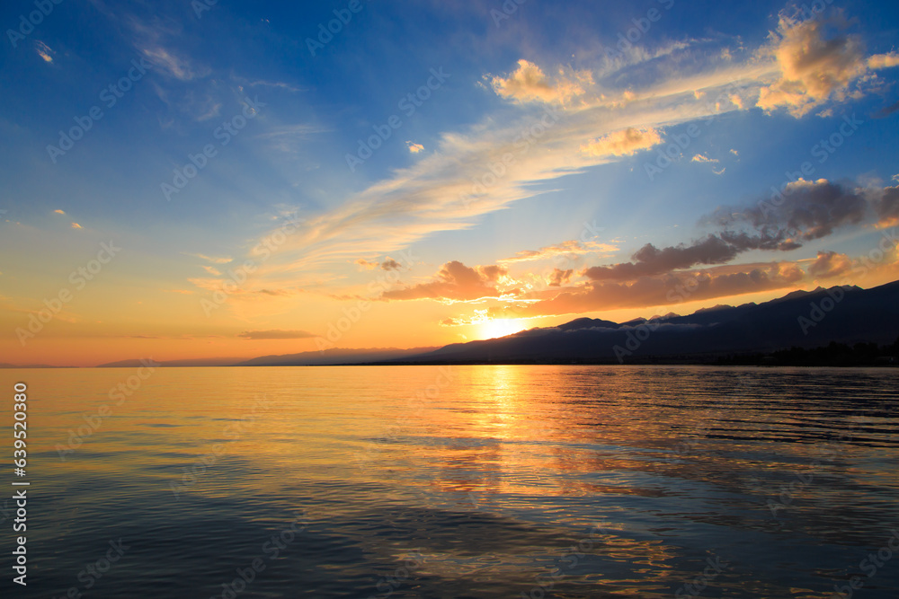 Colorful sunset on the sea. Mountain lake in the rays of the orange sun. Kyrgyzstan, Lake Issyk-Kul.