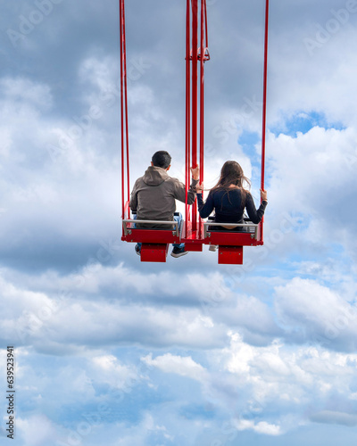 Back rear view of tourist couple on red seesaw swinging high in the air space against beautiful blue sky above the town. Amsterdam, Holland.