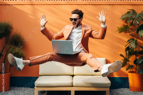 Stylish Influencer Businessman Working on Laptop While Levitating; Zen in Business, Rapid Success and Quick Profit Concept; Against an Orange Wall Background