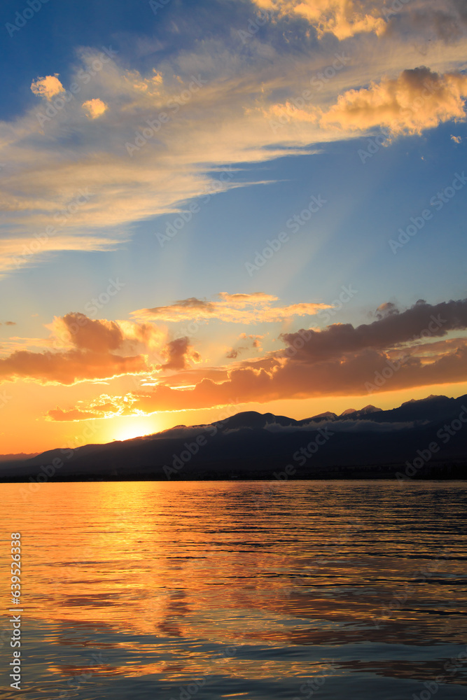Beautiful cloudy sunset over the sea and mountains. Bright sky in the rays of the orange sun. natural texture