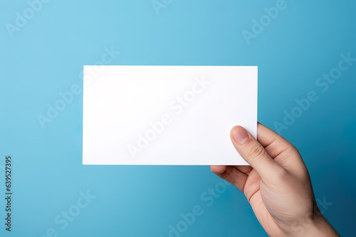 A human hand holding a blank sheet of white paper or card isolated on blue background