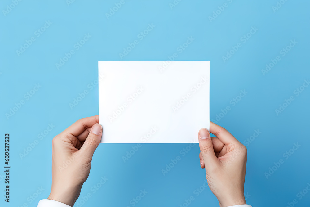A human hand holding a blank sheet of white paper or card isolated on blue background A human hand holding a blank sheet of white paper or card isolated on blue background
