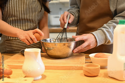 Cropped shot of young couple in apron preparing dough for homemade pancakes, mixing eggs, batter and milk in bowl