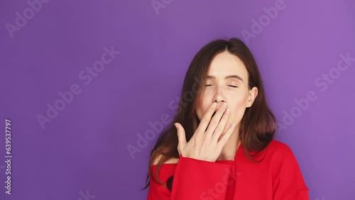 Tired sleepy woman yawns, covers her mouth with hand.Brunette hair girl yaw and cover her mouth. Very boring, uninteresting. Violet studio background.