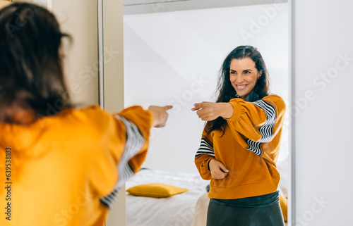 Self confident single woman pointing finger at reflection in mirror dancing and felling good. Independent person with high self esteem talk positive I can do it motivation. © hitdelight